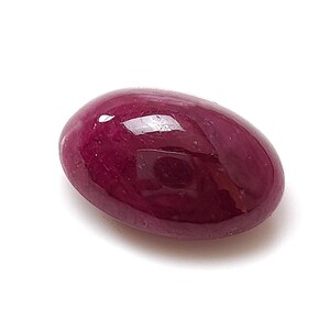 May include: A polished, oval-shaped ruby gemstone. The gem is a deep, rich red color with a smooth, reflective surface. The ruby is set against a white background, highlighting its color and shape. This gemstone is suitable for jewelry making.