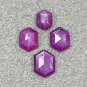 Puede incluir: Cuatro piedras preciosas facetadas de un vibrante tono rosa magenta. Cada piedra está tallada en una forma hexagonal distintiva con una parte superior plana y facetas geométricas simétricas que reflejan la luz, dispuestas en forma de diamante sobre una superficie texturizada.