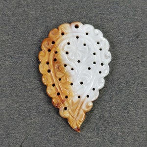 May include: Ornate, teardrop-shaped pendant with a floral design. The pendant features a scalloped edge and is carved with a detailed floral pattern. The color gradient transitions from a warm, amber hue to a bright white. Small holes are evenly spaced throughout the design.