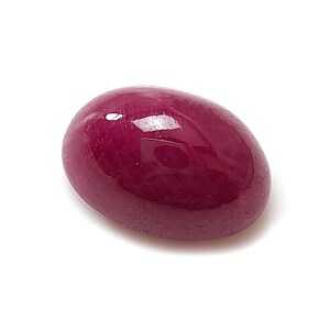 Könnte beinhalten: Ein polierter, oval geformter Rubin-Edelstein. Der Edelstein hat eine tiefe, satte rote Farbe mit einer glatten, reflektierenden Oberfläche. Der Rubin ist vor einem weißen Hintergrund platziert.