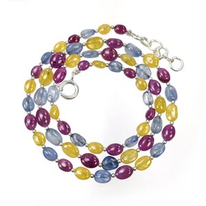 May include: A multi-strand necklace featuring oval-shaped beads in shades of yellow, magenta, and light blue. The beads are separated by small silver-toned metal spacers and the necklace is secured with a silver-toned circular clasp and chain.