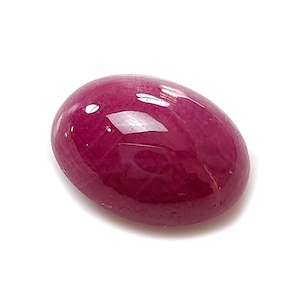 Könnte beinhalten: Ein polierter, ovalförmiger Rubin-Edelstein. Der Edelstein hat eine tiefe, satte rote Farbe mit glänzender Oberfläche. Der Stein ist vor einem weißen Hintergrund platziert, um seine Farbe und Form hervorzuheben. Geeignet für die Schmuckherstellung.