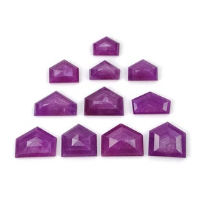 Peut inclure: Une collection de dix pierres précieuses facettées d'une teinte magenta-violet vif. Chaque pierre est taillée en forme de bouclier pentagonal distinct avec une base plate et un sommet pointu, disposées en pyramide sur un fond blanc uni.