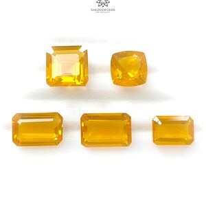 Può includere: Cinque pietre preziose giallo dorato sfaccettate di varie forme sono esposte su sfondo bianco. Le pietre preziose includono tagli quadrati, a cuscino e rettangolari. Il logo Saksham Gems è visibile in alto a destra.