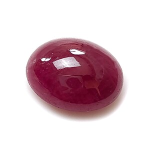 Pode incluir: Uma pedra preciosa de cor vermelho-profundo, de formato oval, com um corte cabochão liso e polido. A superfície da pedra apresenta um acabamento brilhante e reflexivo com reflexos de luz visíveis, exibindo uma cor carmesim rica e saturada.