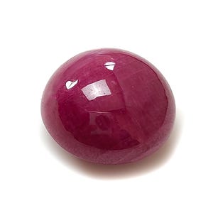 Op de afbeelding: Een gladde, gepolijste, ovaalvormige robijn edelsteen met een diepe magenta-rode kleur. Het oppervlak van de steen is afgerond en vertoont een glanzende, reflecterende afwerking met zichtbare interne insluitingen en lichtreflecties.