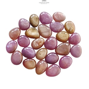 May include: A collection of polished, oval-shaped gemstones in various shades of pink, magenta, and golden-brown. The stones have a smooth, glossy surface and are arranged in a cluster. The text SAKSHAM GEMS THE EFFICACY is visible at the top.