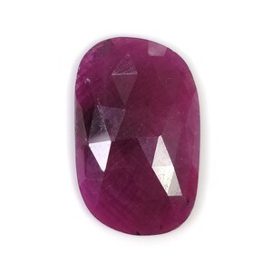 May include: A loose, oval-shaped ruby gemstone with a deep magenta-red hue. The stone features a faceted surface with multiple triangular and geometric cuts that reflect light, creating a polished appearance with visible internal inclusions.