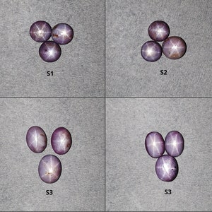 May include: Four sets of three cabochon-cut star sapphires, labeled S1, S2, and S3. Each purple-toned gemstone displays a distinct six-rayed star effect on its smooth, rounded surface. The stones are arranged in small clusters against a gray background.