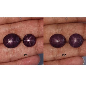 Könnte beinhalten: Zwei Paare ovaler, tiefvioletter Sternsaphire, beschriftet mit P1 und P2. Jeder Cabochon-Edelstein zeigt einen ausgeprägten sechsstrahligen Asterismus-Effekt auf seiner glatten, polierten Oberfläche, der das Licht in einem Stern reflektiert.
