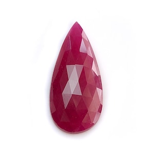 May include: A pear-shaped ruby gemstone with a faceted surface. The stone displays a deep, saturated magenta-red color throughout its body. The geometric facets create a pattern of light and dark reflections across the surface of the gemstone.