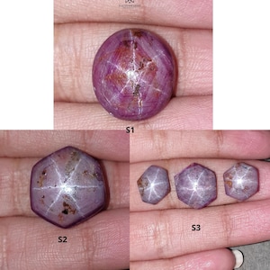 May include: A collection of star ruby gemstones in various shapes. The gemstones range in color from pink to red, with a visible star effect. The stones are displayed on a neutral background, showcasing their natural beauty.