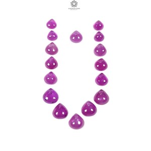 May include: A collection of fifteen loose, teardrop-shaped purple gemstones arranged in a U-shape. Each stone features a smooth, polished surface with a vibrant magenta-purple hue. The logo for Saksham Gems is visible at the top centre.