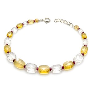 May include: A bracelet featuring alternating faceted yellow and clear rectangular beads, accented with small dark red spherical spacers. The jewelry piece includes a silver-toned metal spring ring clasp and an adjustable chain link extension.