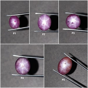 以下が含まれることがあります： 星形の模様がそれぞれ異なる、ピンク色のスターサファイアが5つ、ピンセットで保持されています。サファイアは楕円形で、光沢のある研磨仕上げが施されています。