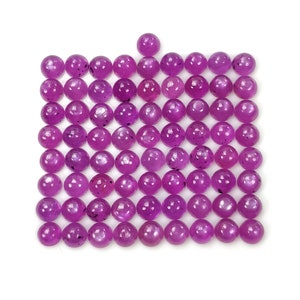Puede incluir: Una cuadrícula de ochenta y una cuentas redondas y pulidas de color magenta dispuestas en formación cuadrada. Cada cuenta presenta una superficie lisa y brillante con sutiles inclusiones oscuras y variaciones naturales en el tono.
