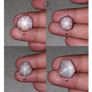 Pode incluir: Quatro safiras estrela hexagonais, cada uma com uma estrela de seis pontas no centro, são exibidas em uma mão. As safiras são de cor púrpura claro com uma estrela branca.