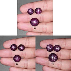 May include: Three sets of star ruby cabochons, each set with two smaller stones and one larger stone. The stones are a deep purple-red color with a star-like pattern.
