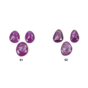 Puede incluir: Tres cabujones de piedra preciosa facetados de color púrpura, dos están en una disposición triangular y uno está debajo de ellos. Los cabujones están etiquetados como S1 y S2.