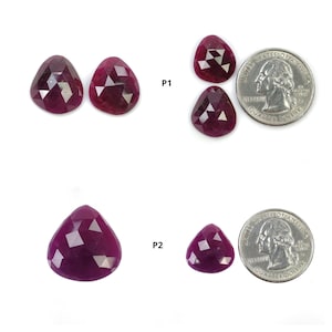 May include: Several faceted, deep red ruby gemstones in various sizes. Two quarters are included for size comparison. The gemstones have a triangular or teardrop shape and are displayed against a white background.