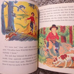 May include: An illustration from a vintage children's book shows a boy in a red shirt and cowboy hat, with a dog, in a forest. The artwork uses bright colours and depicts a narrative scene.