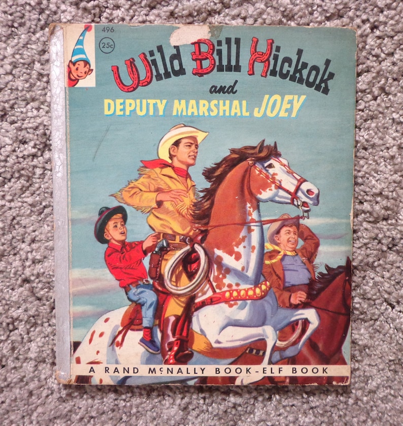 May include: A vintage children's book titled "Wild Bill Hickok and Deputy Marshal Joey." The cover illustration depicts cowboys on horseback. The book is a Rand McNally Book-Elf Book.