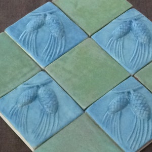 May include: Six square ceramic tiles with a repeating pattern of two stylized pine cones with needles. The tiles alternate between a light blue and a light green glaze.