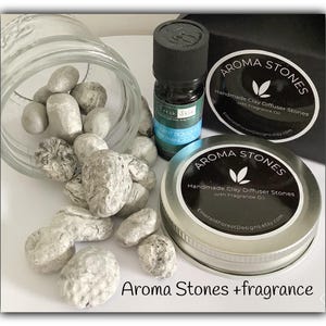 May include: A set of white clay diffuser stones in a glass jar with a small bottle of essential oil. The label on the bottle reads "Fresh Skin" and "Scent Bouquet Fragrance Oil". The jar and bottle are sitting on a black surface with a silver lidded container that reads "Aroma Stones Handmade Clay Diffuser Stones with Fragrance Oil EmeraldForestDesigns.etsy.com".