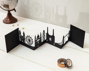 May include: Black paper cut-out London skyline with iconic landmarks like Big Ben, the London Eye, and Tower Bridge. The skyline is folded into a zig-zag pattern.
