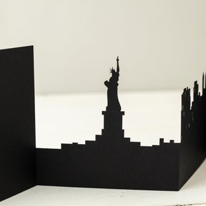 May include: Black paper cutout of the New York City skyline, featuring the Statue of Liberty and skyscrapers.