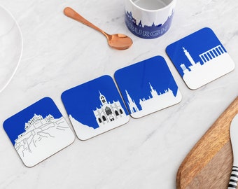 May include: Four blue and white coasters with different images of Edinburgh landmarks. The coasters are on a white surface.