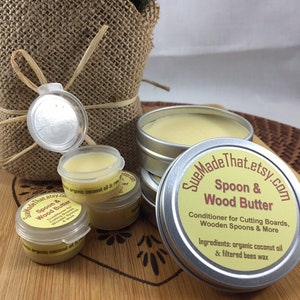 May include: A set of small silver tins filled with a white, creamy substance labeled "Spoon & Wood Butter". The label also states "Conditioner for Cutting Boards, Wooden Spoons & More" and lists the ingredients as "organic coconut oil & filtered bees wax".