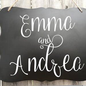 Puede incluir: Se&ntilde;al negra de pizarra con letras blancas en cursiva que dice "Emma y Andrea".