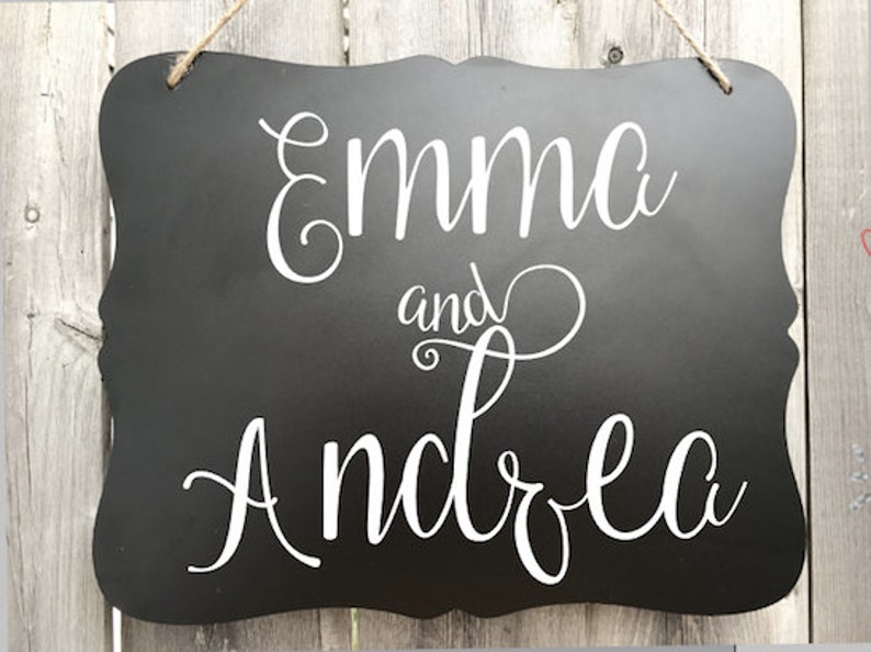 Puede incluir: Se&ntilde;al negra de pizarra con letras blancas en cursiva que dice "Emma y Andrea".