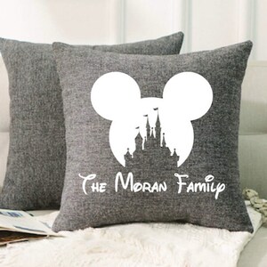 May include: Two gray throw pillows with a white silhouette of Mickey Mouse's head with the iconic Disney castle inside. The text "The Moran Family" is printed below the silhouette.