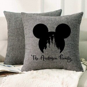May include: Gray throw pillows with a black silhouette of Mickey Mouse ears and Cinderella's castle inside the ears. The text "The Anderson Family" is printed below the silhouette.
