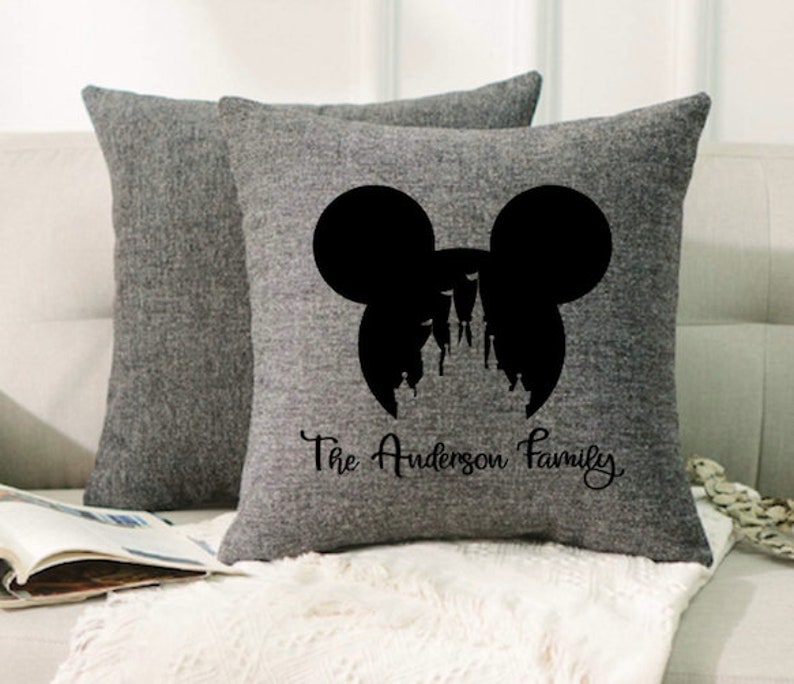 May include: Gray throw pillows with a black silhouette of Mickey Mouse ears and Cinderella's castle inside the ears. The text "The Anderson Family" is printed below the silhouette.