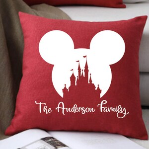 May include: Red throw pillow with a white silhouette of Mickey Mouse ears and Cinderella's castle inside the ears. The text "The Anderson Family" is printed below the silhouette.