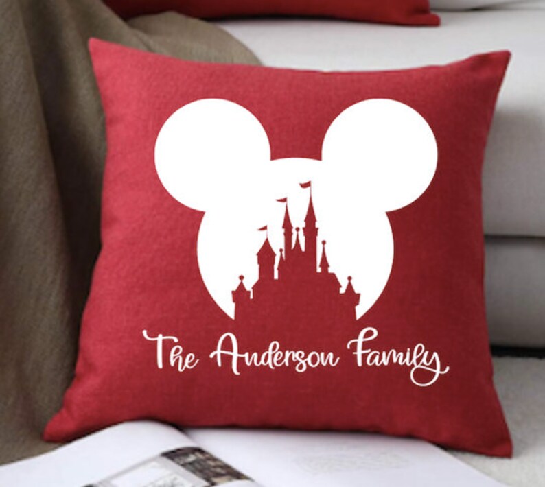 May include: Red throw pillow with a white silhouette of Mickey Mouse ears and Cinderella's castle inside the ears. The text "The Anderson Family" is printed below the silhouette.