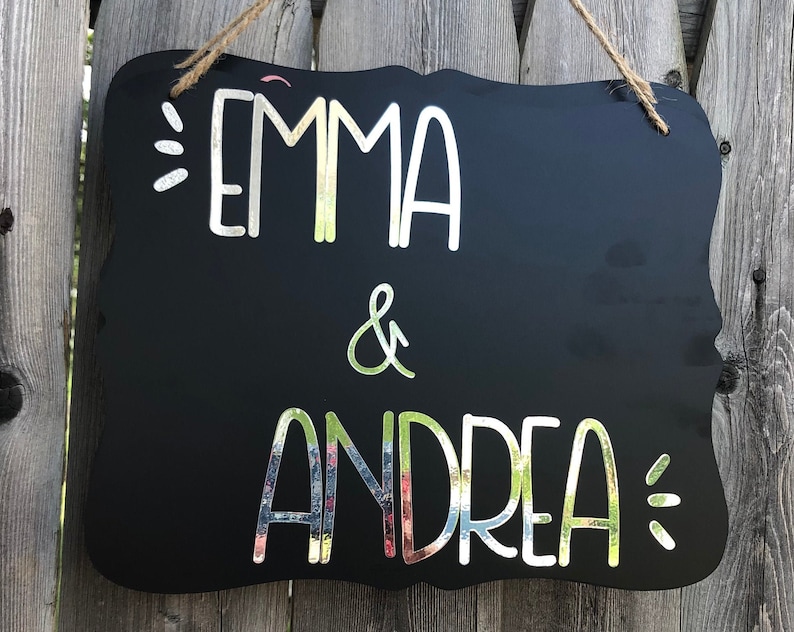 Puede incluir: Se&ntilde;al negra de pizarra con letras blancas que dice "Emma & Andrea" con acentos decorativos.