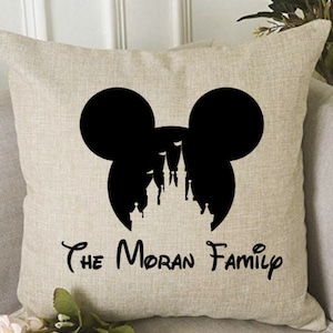 May include: A beige throw pillow with a black silhouette of Mickey Mouse ears with Cinderella's castle inside. The text "The Moran Family" is printed below the silhouette.