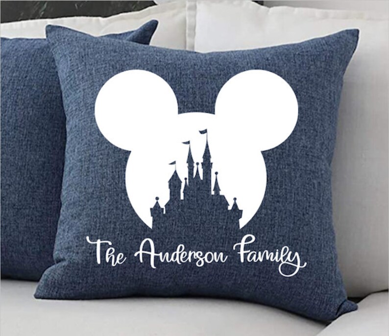 May include: A blue throw pillow with a white silhouette of Mickey Mouse's head with Cinderella's castle inside. The text "The Anderson Family" is printed below the silhouette.