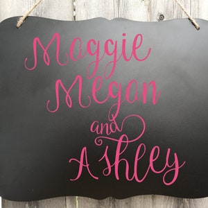 Puede incluir: Se&ntilde;al negra de pizarra con una inscripci&oacute;n cursiva rosa que dice "Maggie Megan y Ashley".
