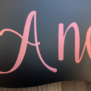 Puede incluir: Un letrero negro con la palabra "Andrea" escrita en letras cursivas doradas.