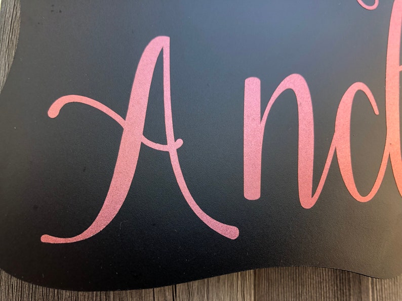 Puede incluir: Un letrero negro con la palabra "Andrea" escrita en letras cursivas doradas.