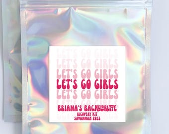 May include: A holographic iridescent zippered pouch with a pink and white sticker that says "Let's Go Girls" repeated four times. The sticker also includes the text "Briana's Bachelorette Recovery Kit Savannah 2023".