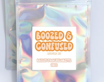 May include: A silver iridescent zippered pouch with a white label that reads "Boozed & Confused" with a peach-colored font. The label also includes the text "August 24th, Bailey's Bachelorette 2023".