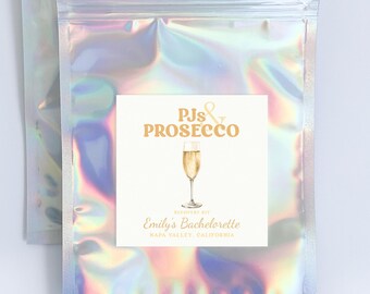 May include: A silver iridescent zippered pouch with a white square label that says "PJs & PROSECCO" in orange text with a gold champagne flute illustration. The label also says "celebrating at Emily's Bachelorette Napa Valley, California."