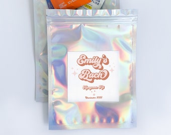 May include: A silver iridescent zippered pouch with a white label that says "Emily's Bach Hangover Kit Charleston 2023". The pouch contains various items, including a Tide to-go stain remover wipe, a Liquid I.V. hydration multiplier packet, and an Advil pain reliever packet.