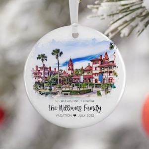 May include: A white round ornament with a watercolor painting of a red brick building with palm trees and a fountain. The text "St. Augustine, Florida The Williams Family Vacation ♥ July 2022" is printed on the ornament.
